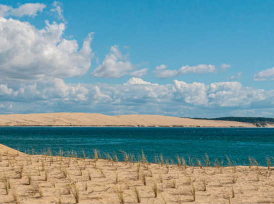 Vue panoramique spectaculaire sur les eaux bleues du Bassin d'Arcachon et la Dune du Pilat à l'horizon, illustrant l'expérience visuelle d'une véritable chambre avec vue mer sans vis-à-vis