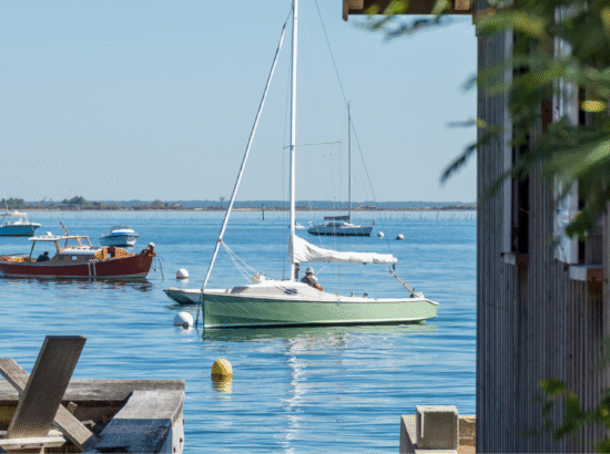 Vue panoramique sur les bateaux et l'eau calme du Bassin d'Arcachon au matin, le cadre idéal pour un petit-déjeuner face à la mer